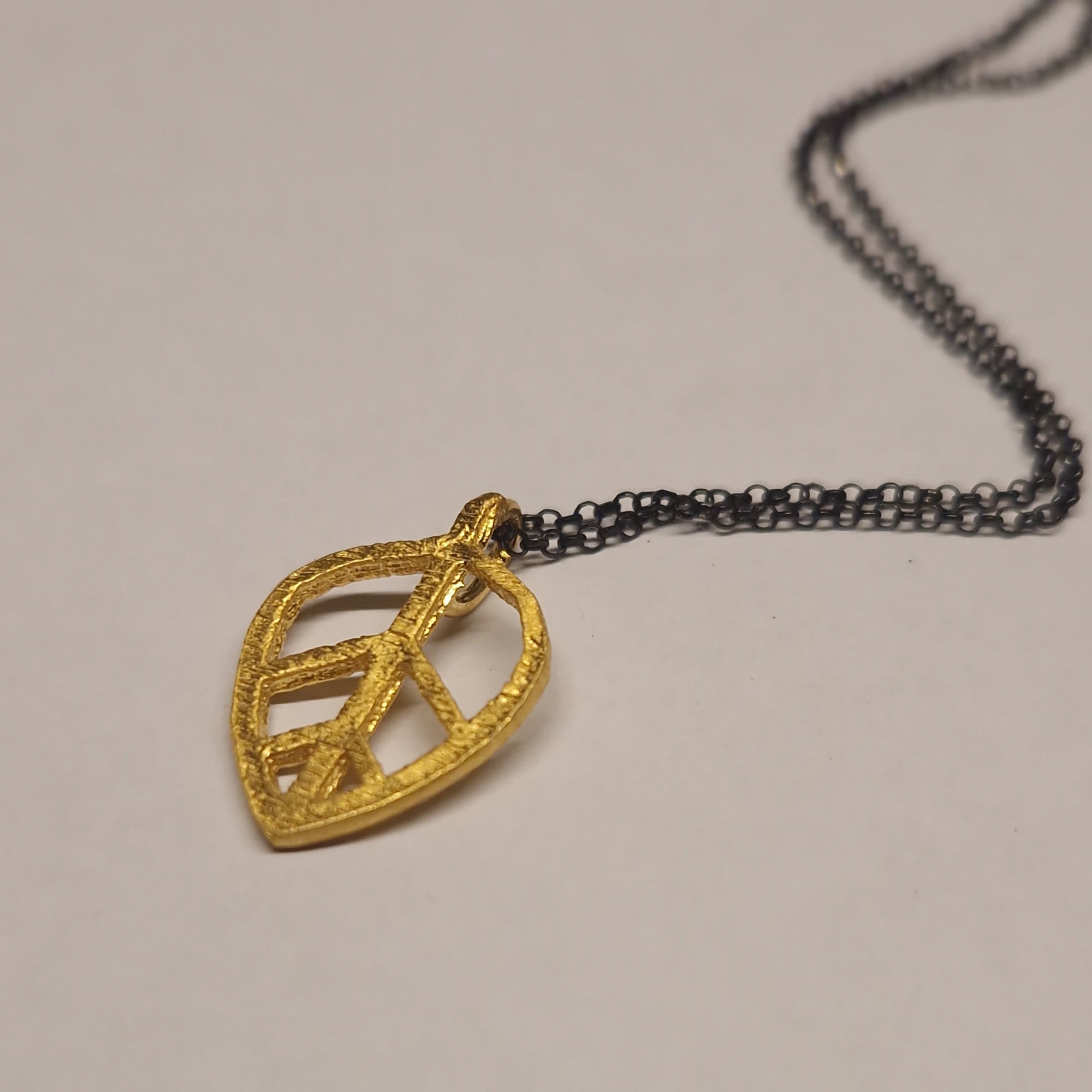 Gold leaf-shaped pendant on a chain against a beige background