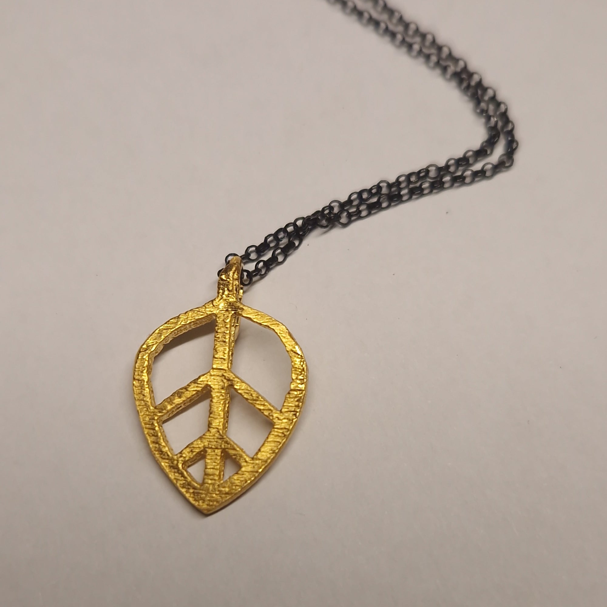 Gold peace symbol pendant on a chain against a beige background