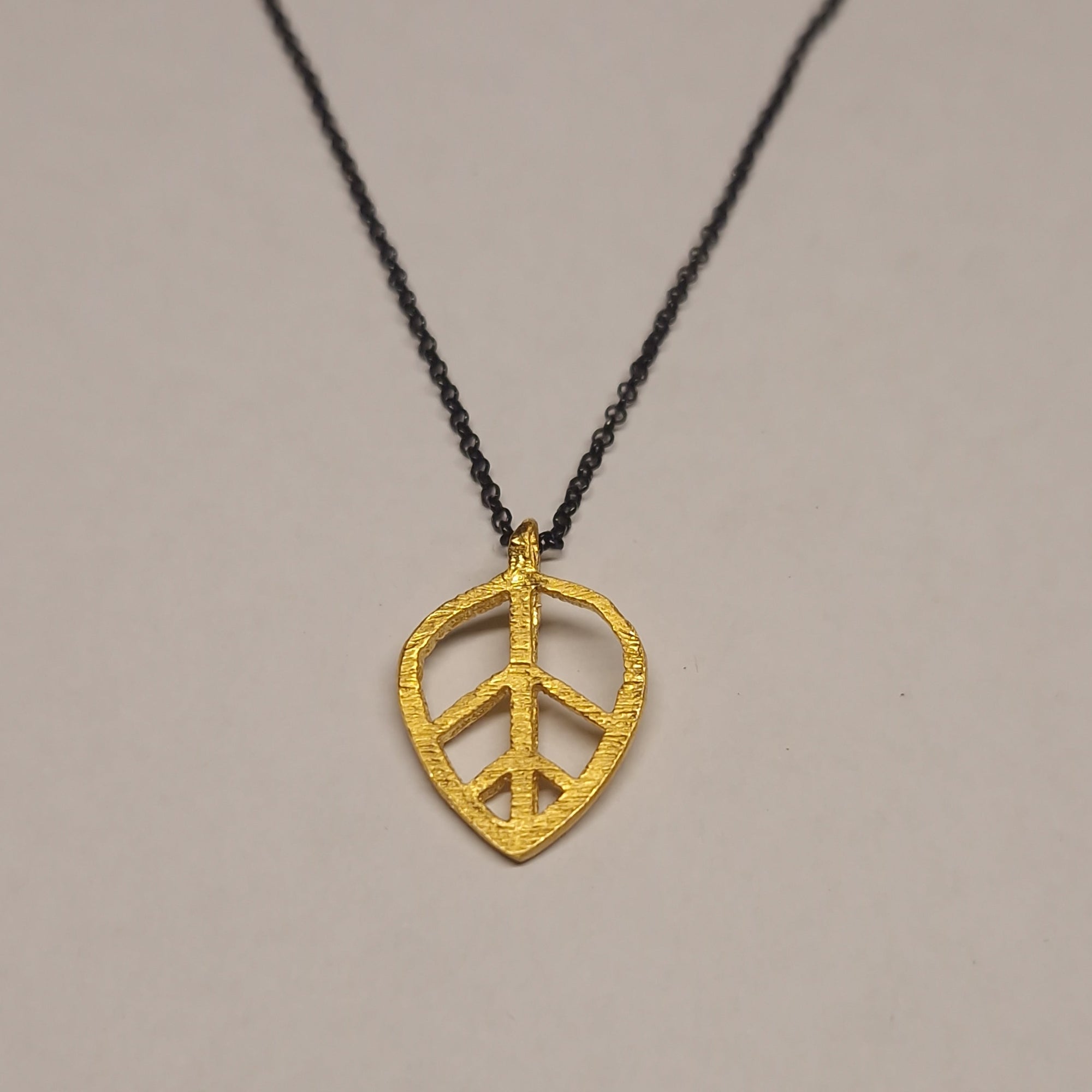 Gold leaf-shaped pendant on a black cord against a gray background