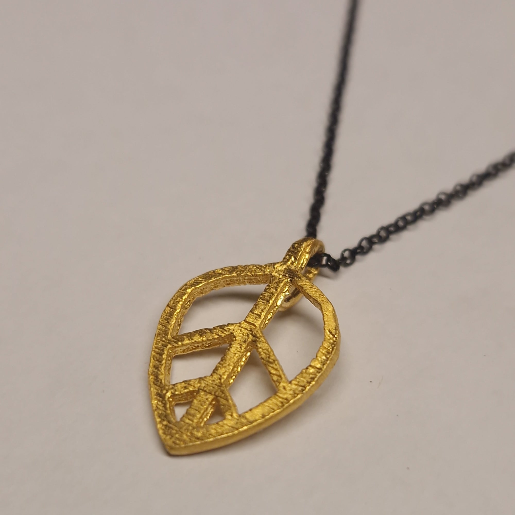 Gold leaf-shaped pendant on a black chain against a neutral background