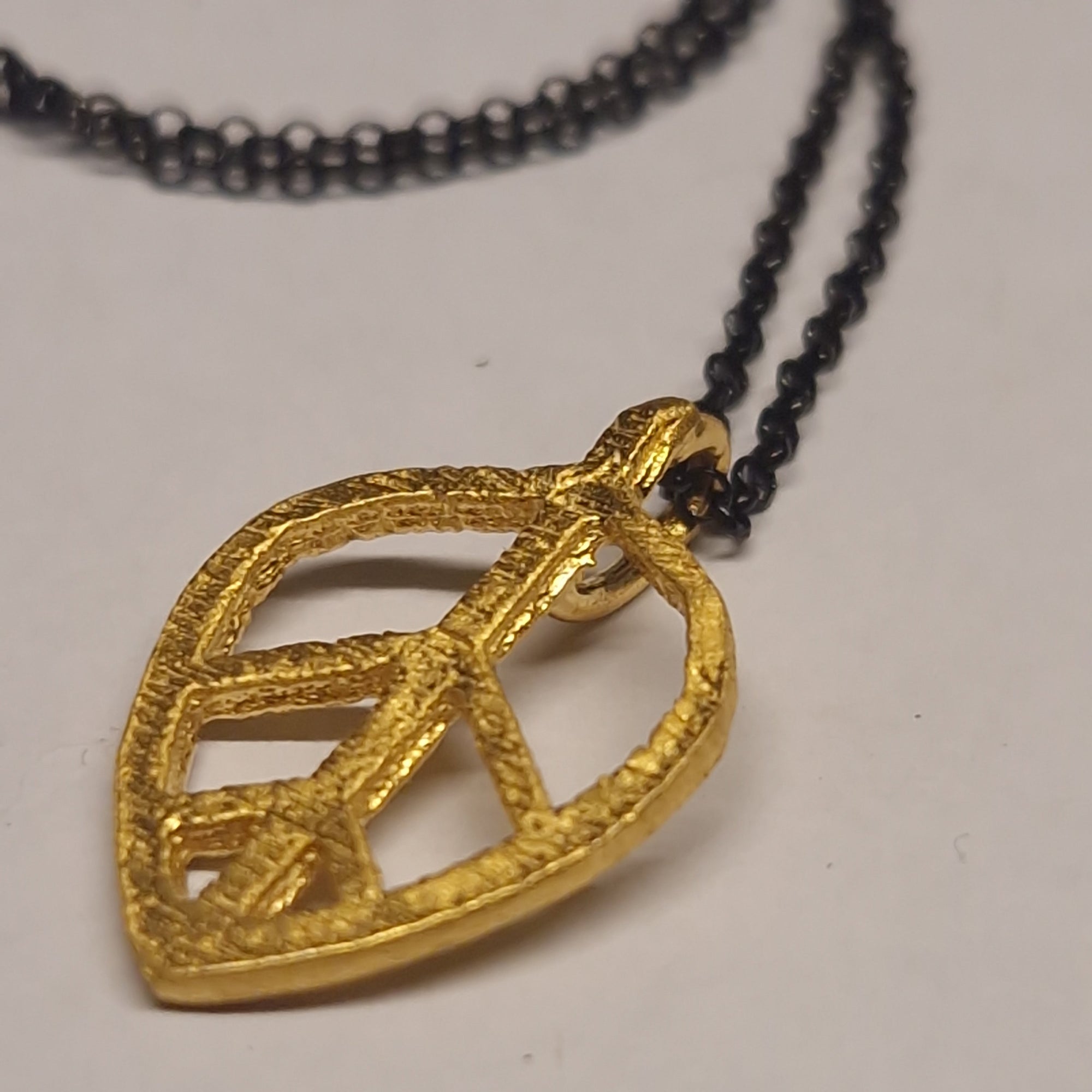Gold leaf-shaped pendant on a black chain against a white background