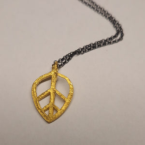 Gold peace symbol pendant on a chain against a beige background