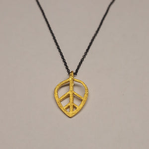 Gold leaf-shaped pendant on a black cord against a gray background