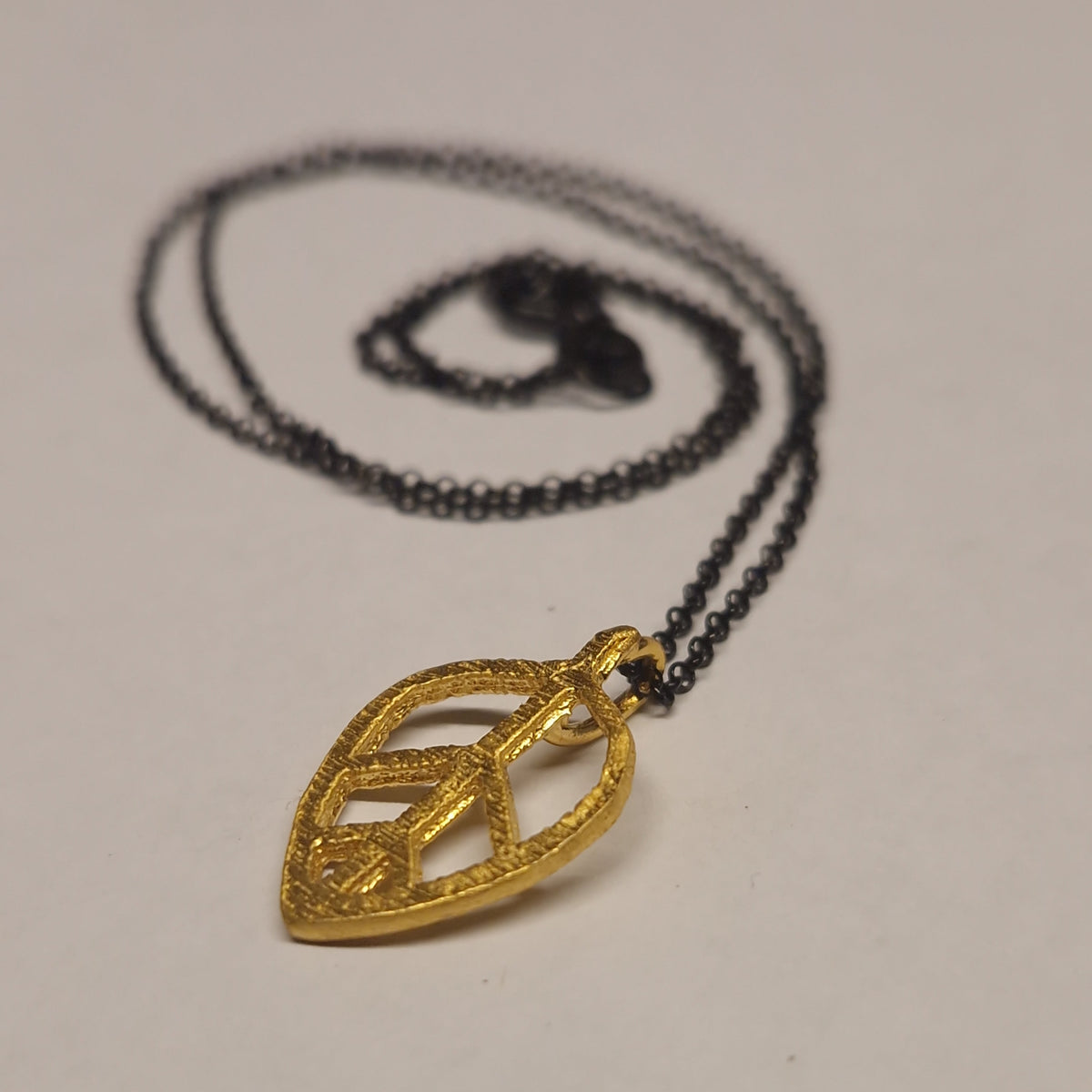 Gold pendant on a black chain against a plain background