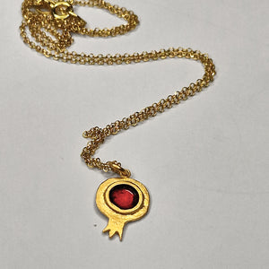Gold necklace with a red gemstone pendant on a light gray background