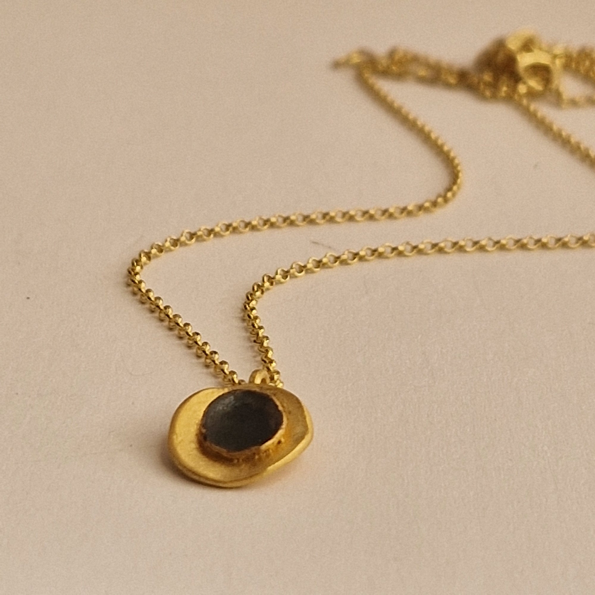 Gold necklace with a black pendant on a beige background