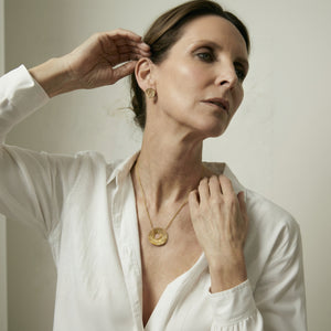 Woman wearing gold jewelry, including earrings and a necklace, against a neutral background.