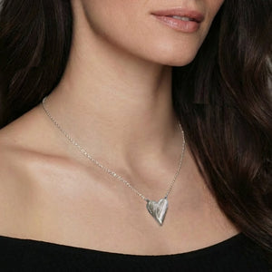 Woman wearing a silver necklace with a heart pendant against a neutral background