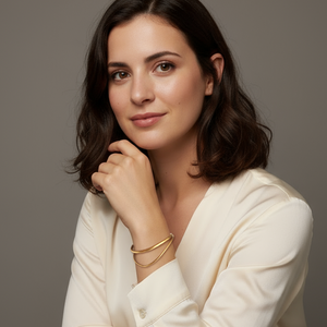 Woman wearing a white blouse and a gold-plaited bracelet, in a gray background. 