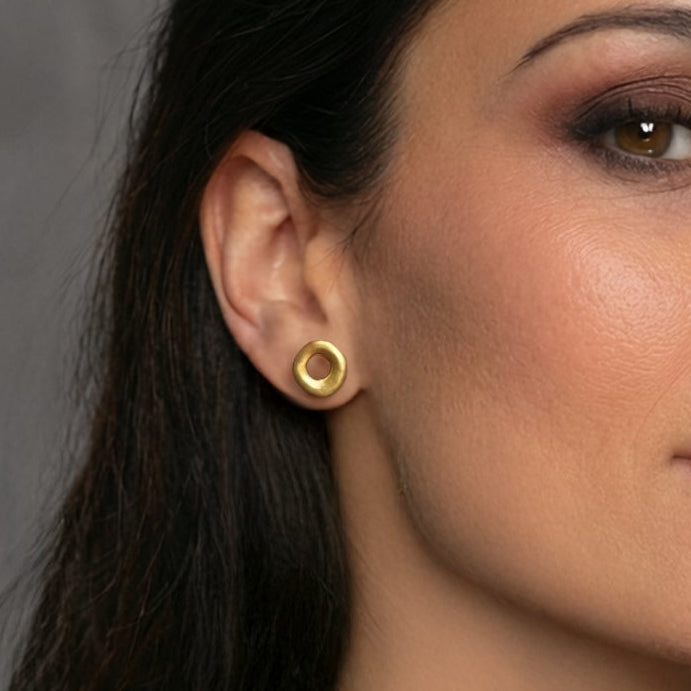 Woman with dark hair and gold earrings against a gray background