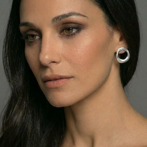 Woman with dark hair and earrings against a neutral background
