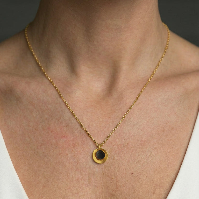 Gold necklace with a black pendant on a person wearing a white top.