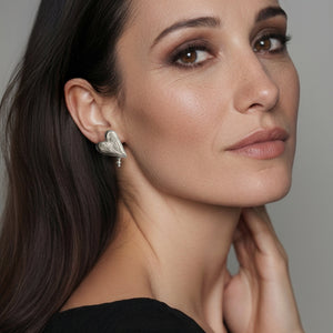 Woman wearing a heart-shaped earring with a dangling pearl, against a neutral background