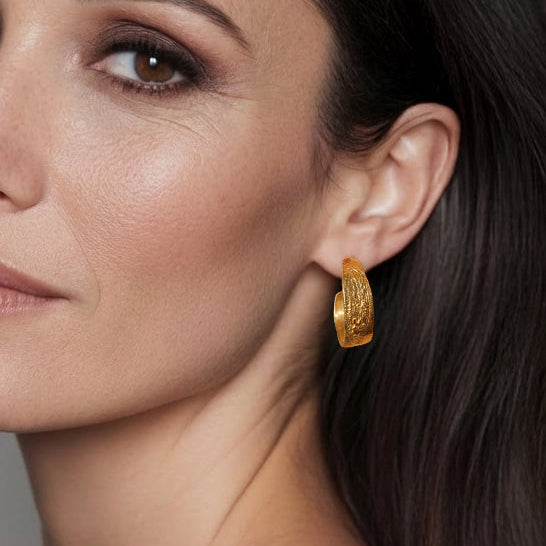 Close-up of a woman wearing gold hoop earrings with a neutral background
