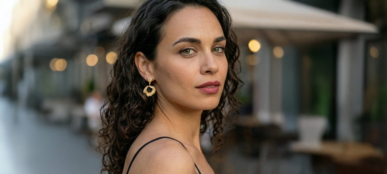 Woman with curly hair and earrings standing outdoors with blurred background